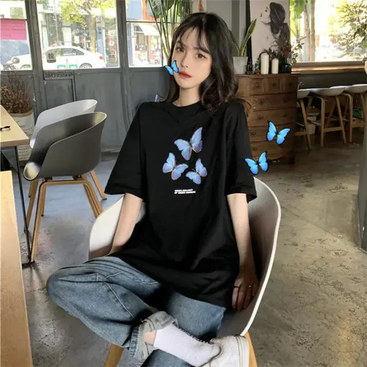 Woman wearing a black short sleeve t-shirt for women with butterfly print, sitting in a stylish café.