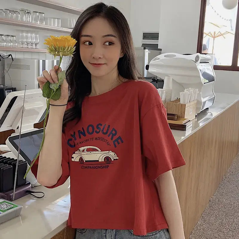 Short Sleeve T-Shirt for Women worn by a woman holding a flower in a cozy cafe setting.