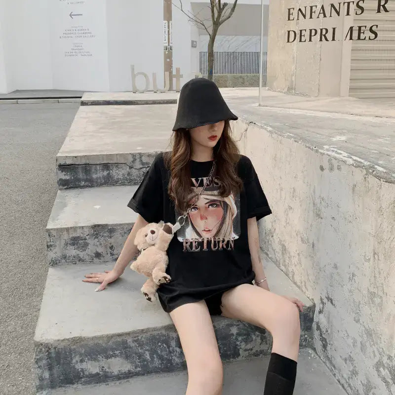 Short Sleeve T-Shirt for Women worn by a model sitting on steps, holding a teddy bear and wearing a hat.