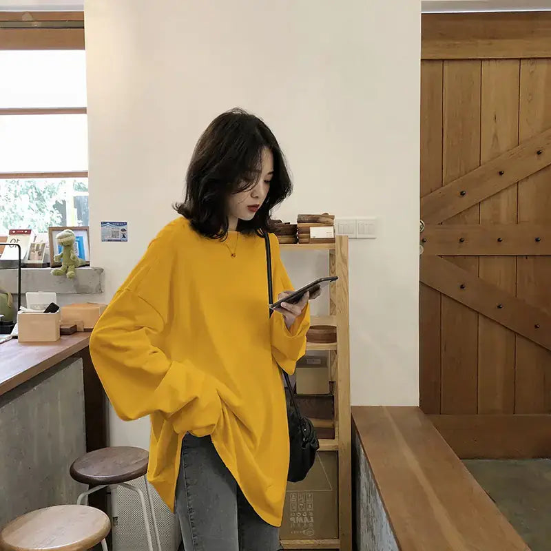 Chic Long Sleeve T-Shirt-Loose Fit Style in yellow, worn casually while using a phone in a cozy setting.
