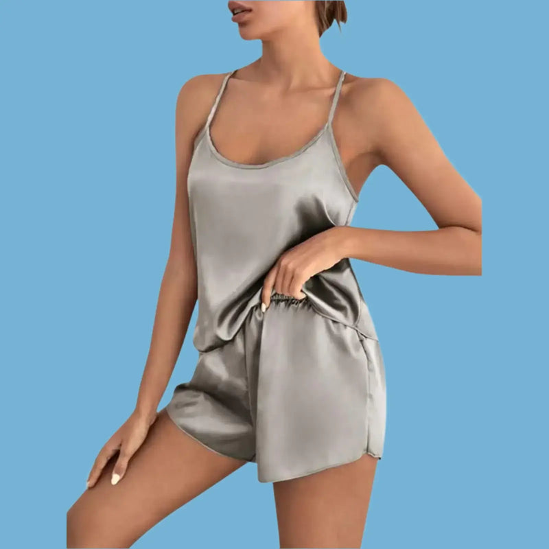 Woman modeling a stylish satin loungewear set in grey, featuring a camisole and shorts, against a light blue background.