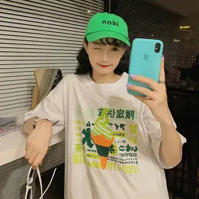 Short Sleeve Women's T-Shirt featuring a fun graphic design, worn by a model with a green cap and smartphone.