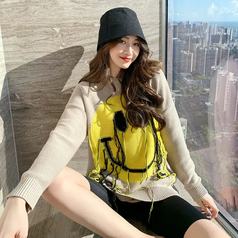 Woman wearing Women's Blissful Smile Pattern Sweater with a smiley design, sitting by a window with a city view.